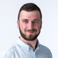 Portrét usmievajúceho muža v modrej košeli odfotený na bielom pozadí.